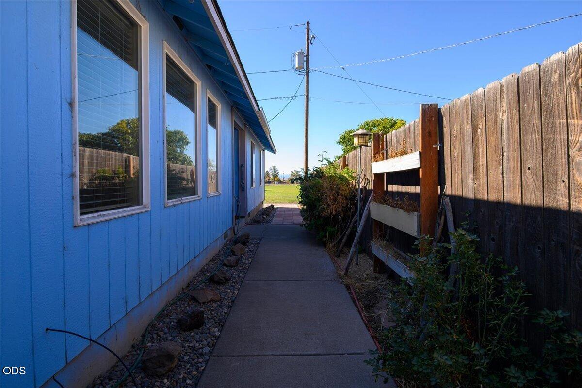 Blue-sided home beside a concrete walkway and tall wooden fence.