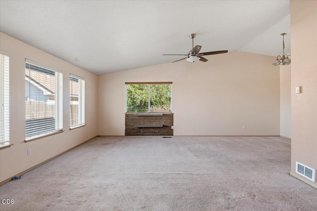Empty living room with carpet, a ceiling fan, and a wooden built-in beneath the rear window.