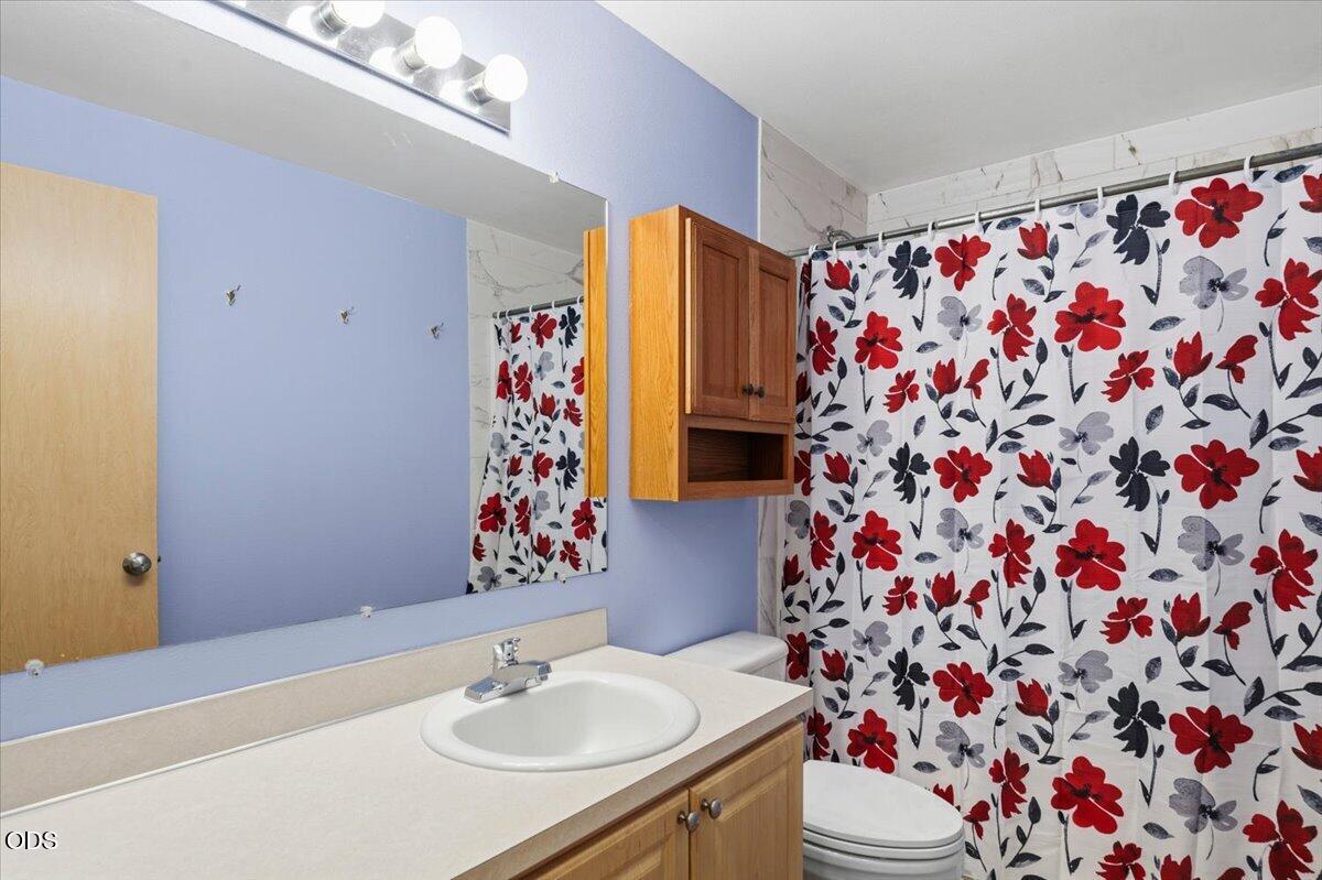 Bathroom with a wood vanity and a bold red-and-black floral shower curtain.