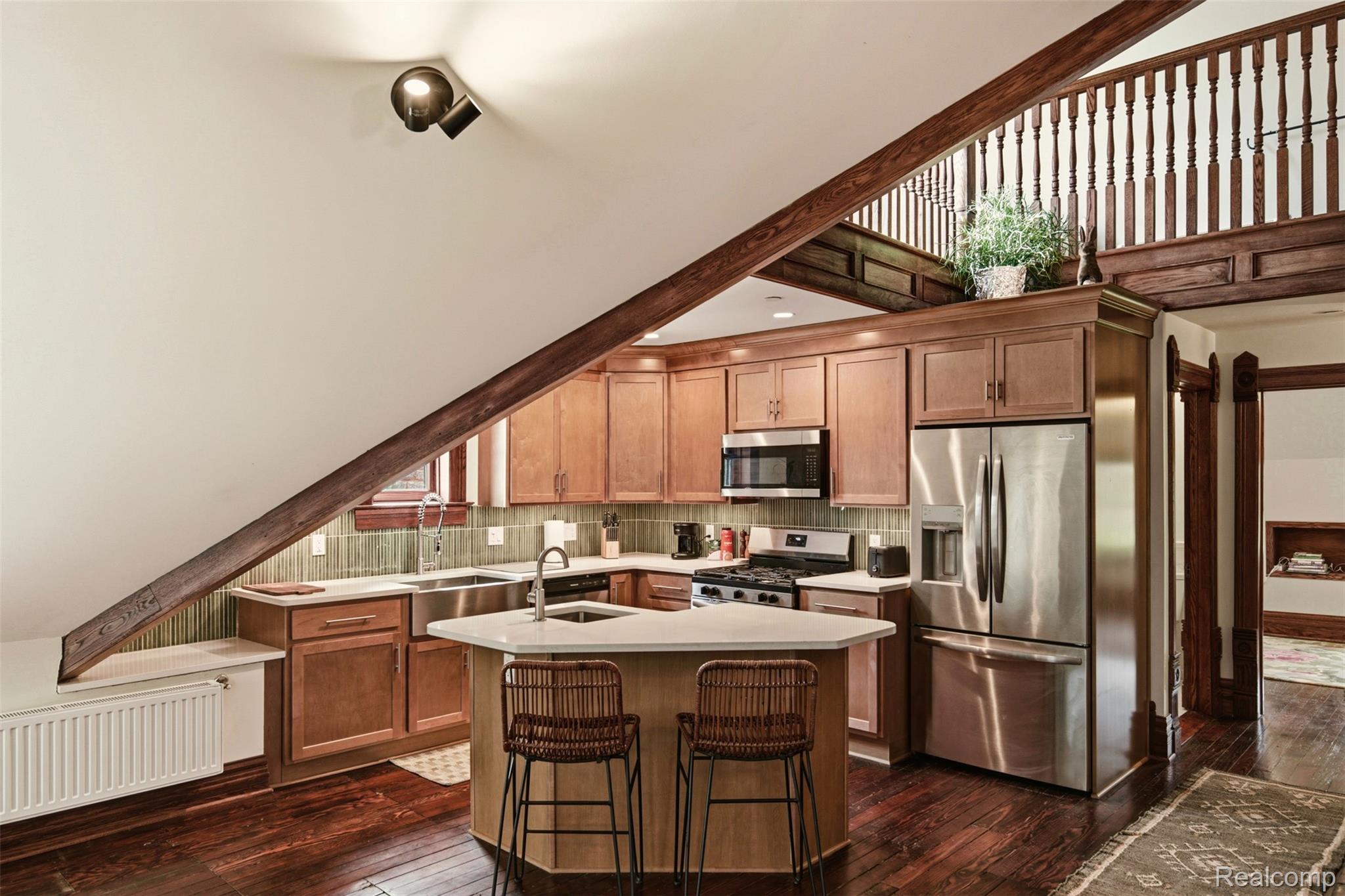Loft kitchen with a wood-railed upper level, stainless steel appliances, and a central island with two stools.