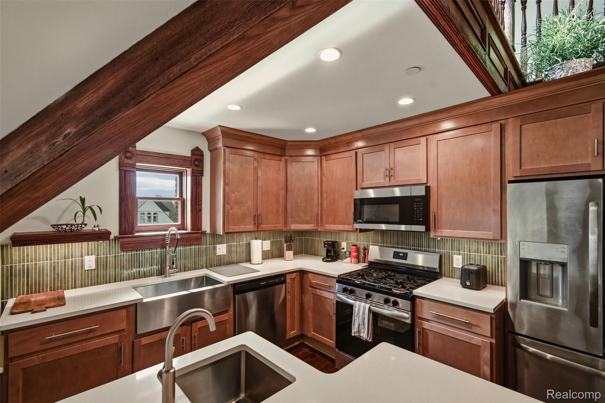 Kitchen with reddish-brown cabinetry, exposed wood beams, stainless steel appliances, and a large island sink.