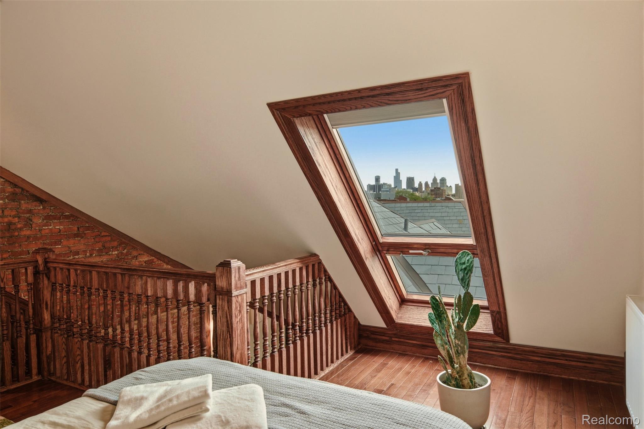 Loft bedroom with a large skylight framing the Detroit skyline and a wooden staircase.