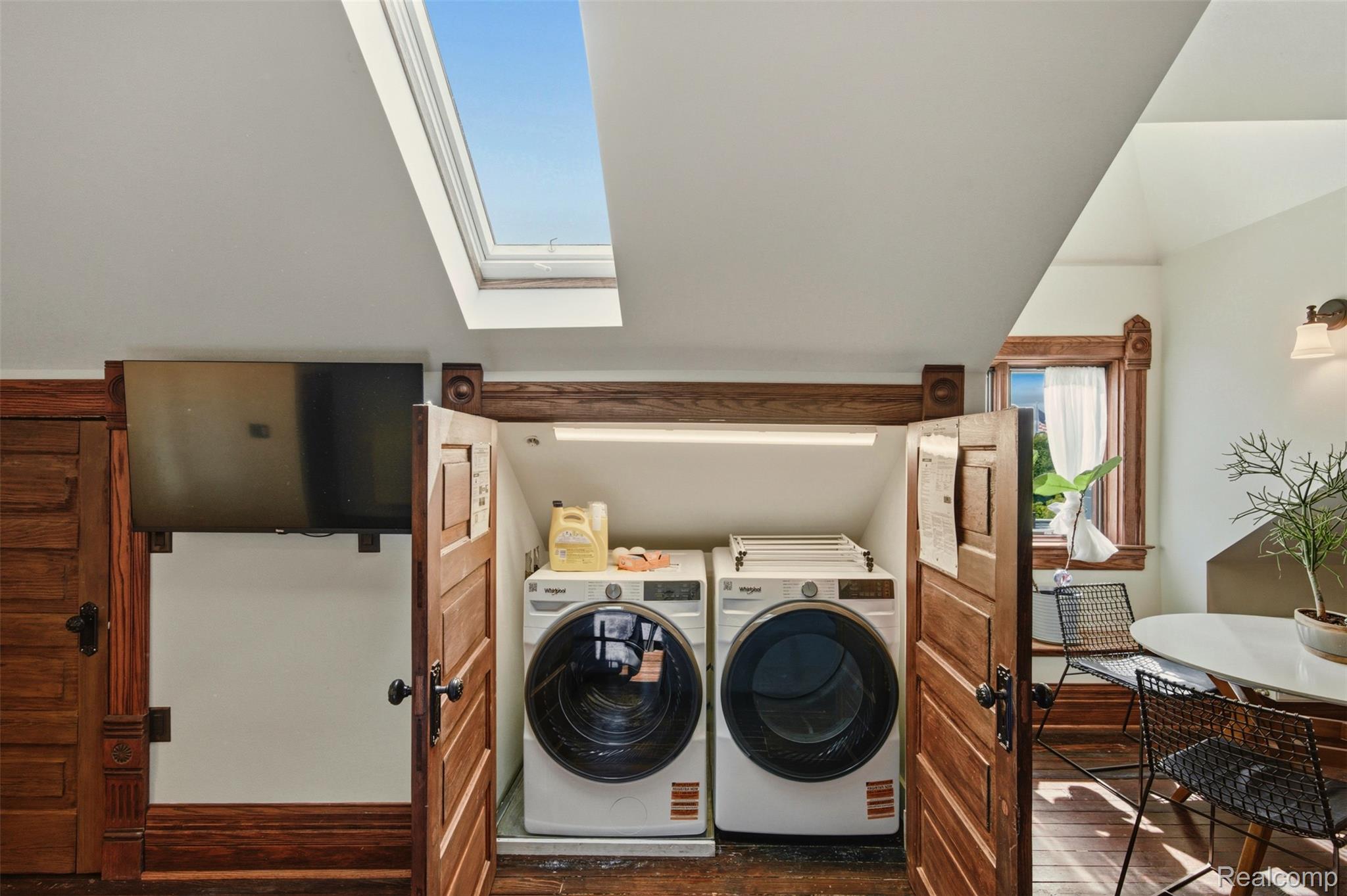 Laundry area with front-loading washer and dryer, open wood doors, and a skylight.