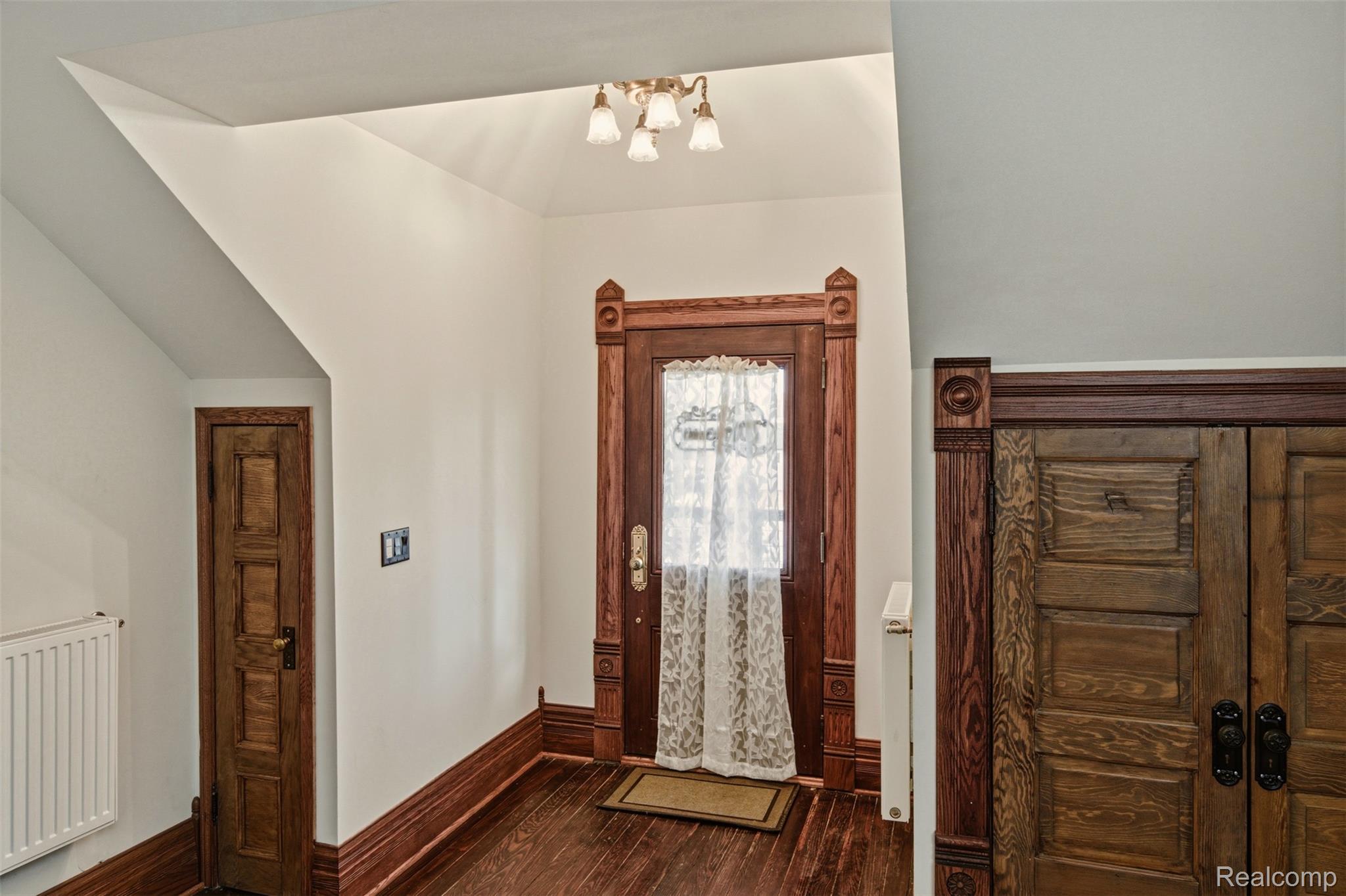 Entry foyer with ornate wood doors, dark hardwood floors, and a curtained glass entry door.
