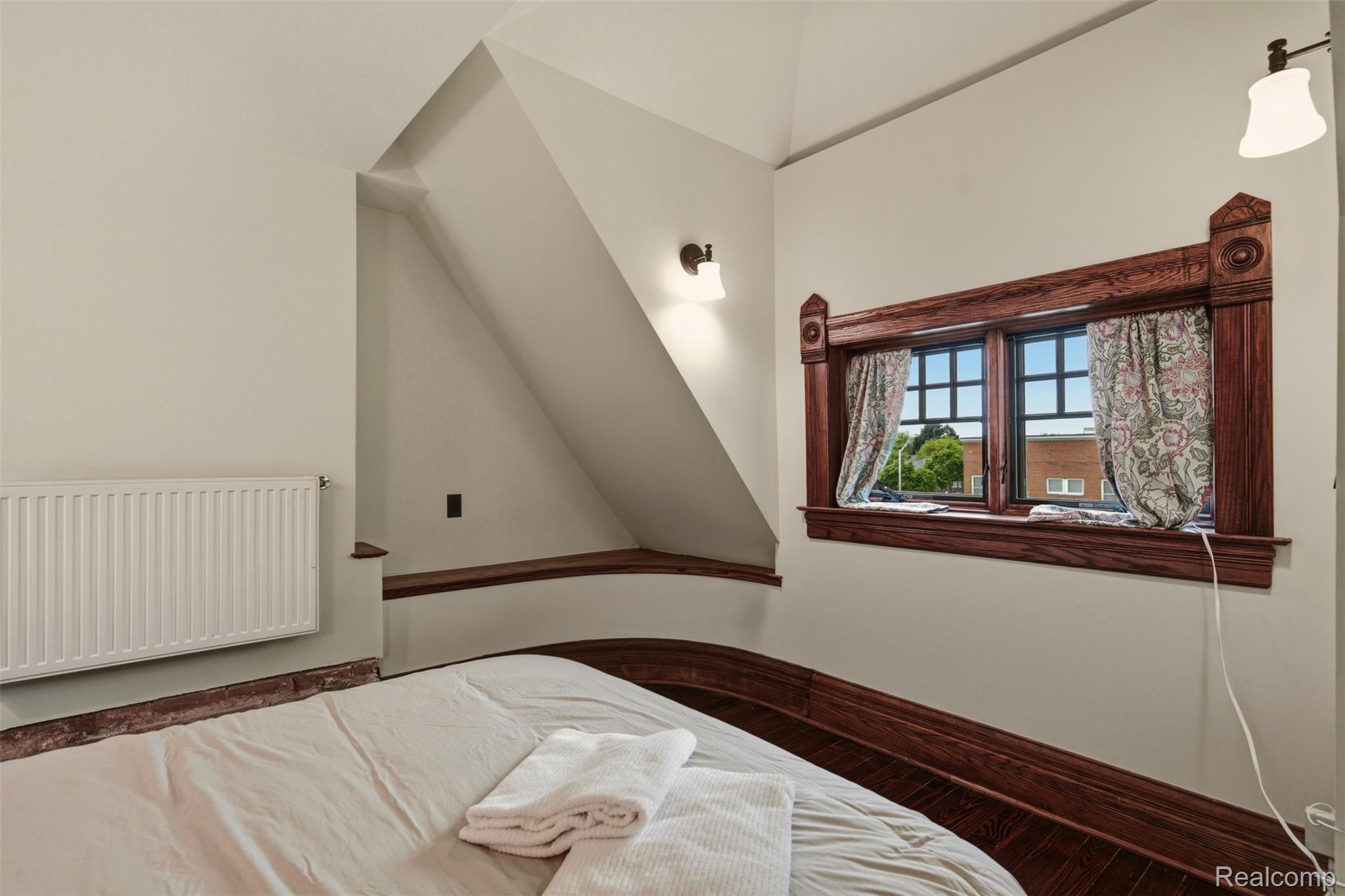 Bedroom with sloped ceiling, white bedding, radiator, and ornate wood-trimmed window.