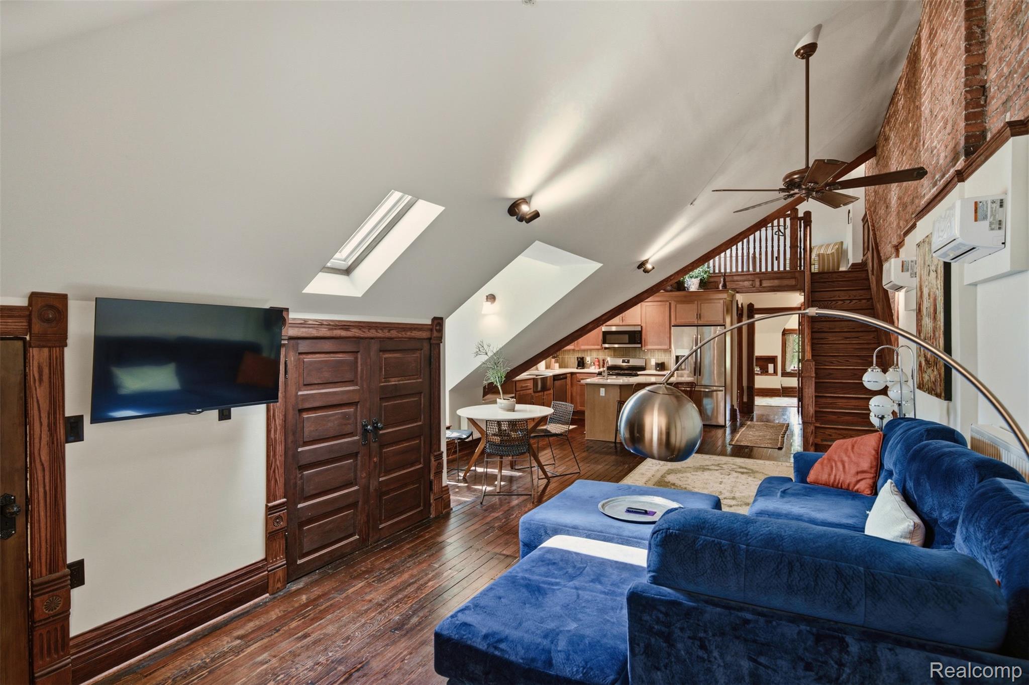 Loft living room with a blue sectional, skylights, exposed brick, and a staircase beside the open kitchen.