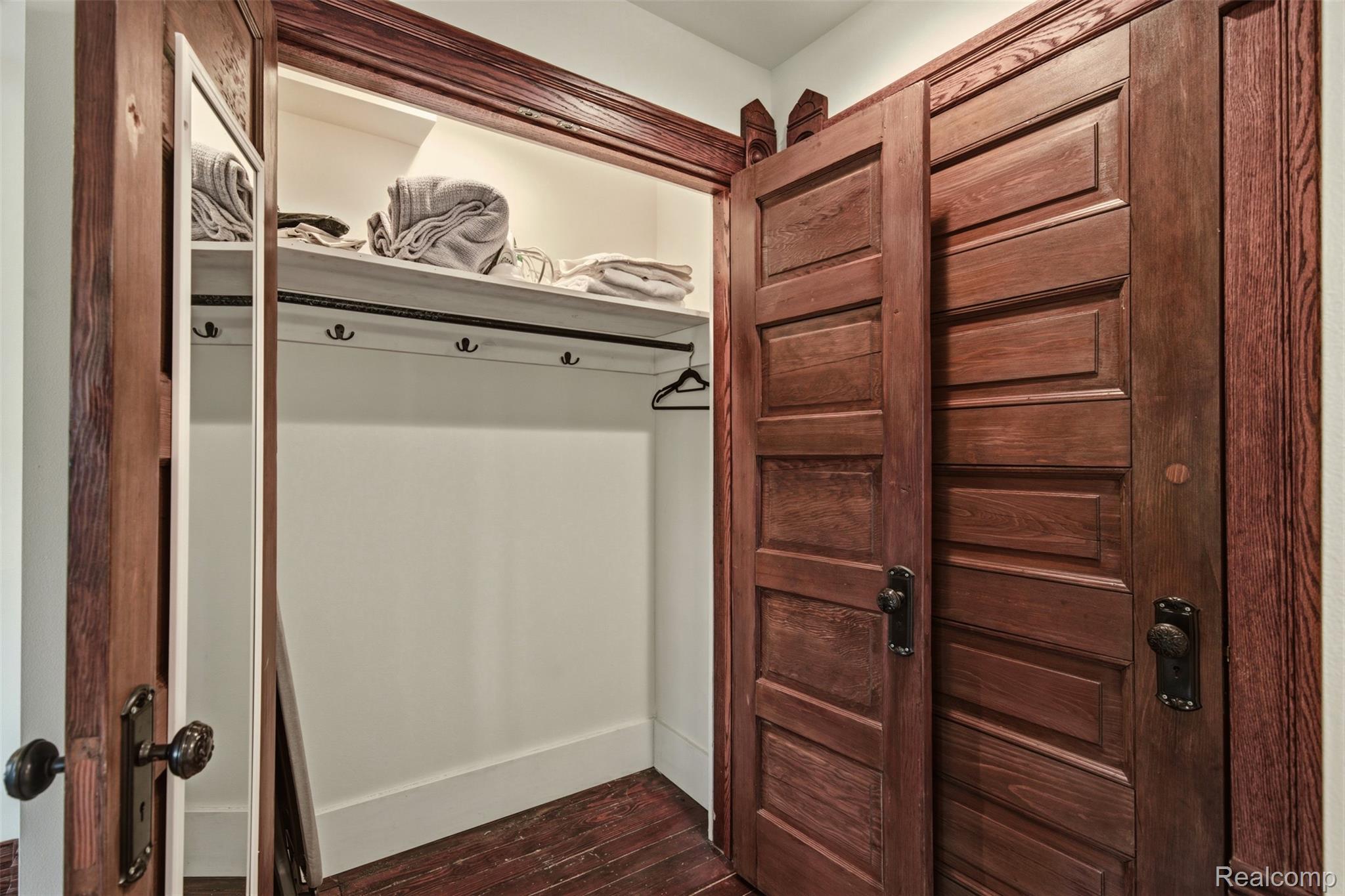 Closet with folded towels, wall hooks, and dark wood paneled doors.