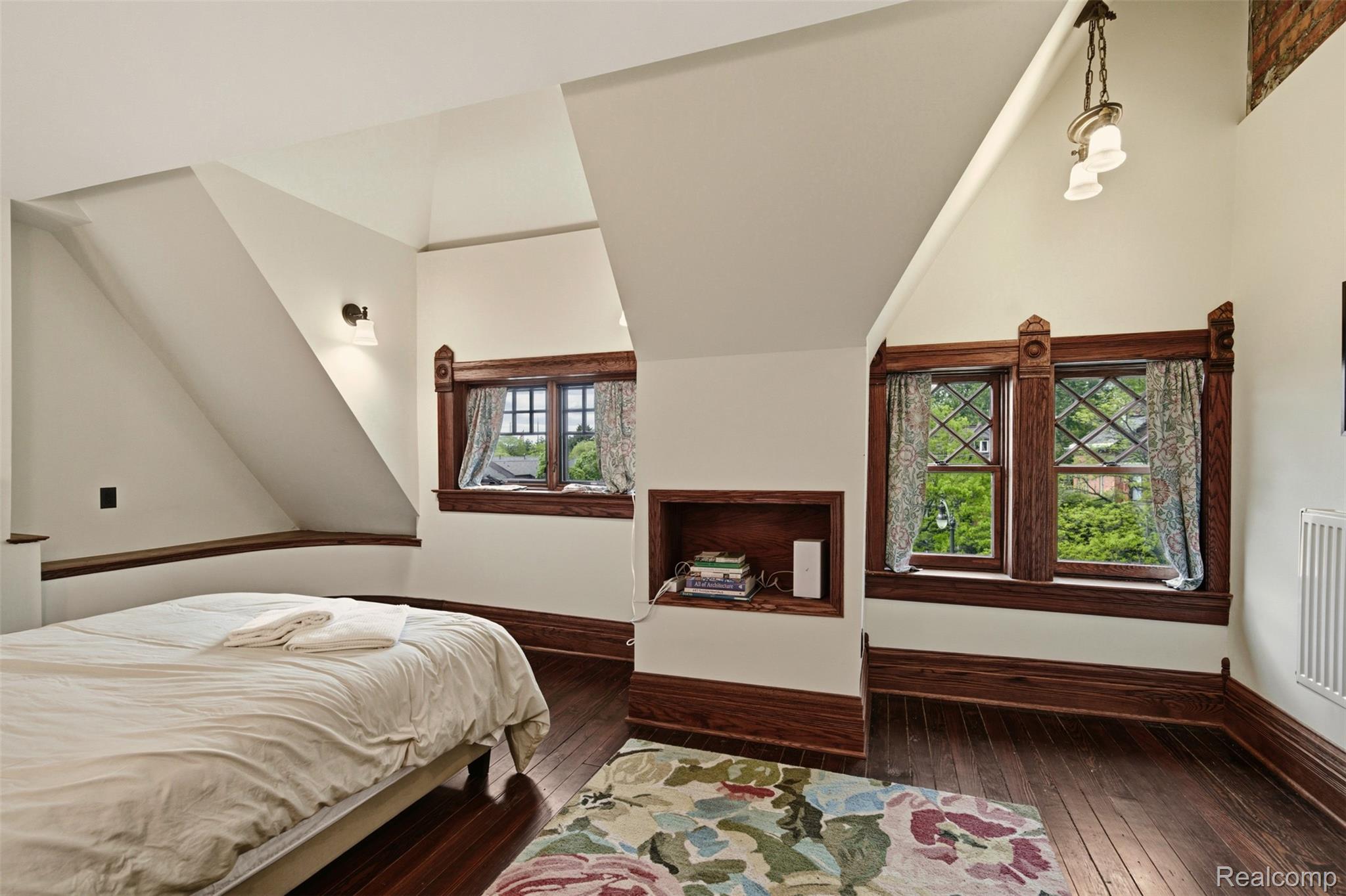 Bedroom with a sloped ceiling, dark wood trim, diamond-pane windows, and a colorful floral rug.
