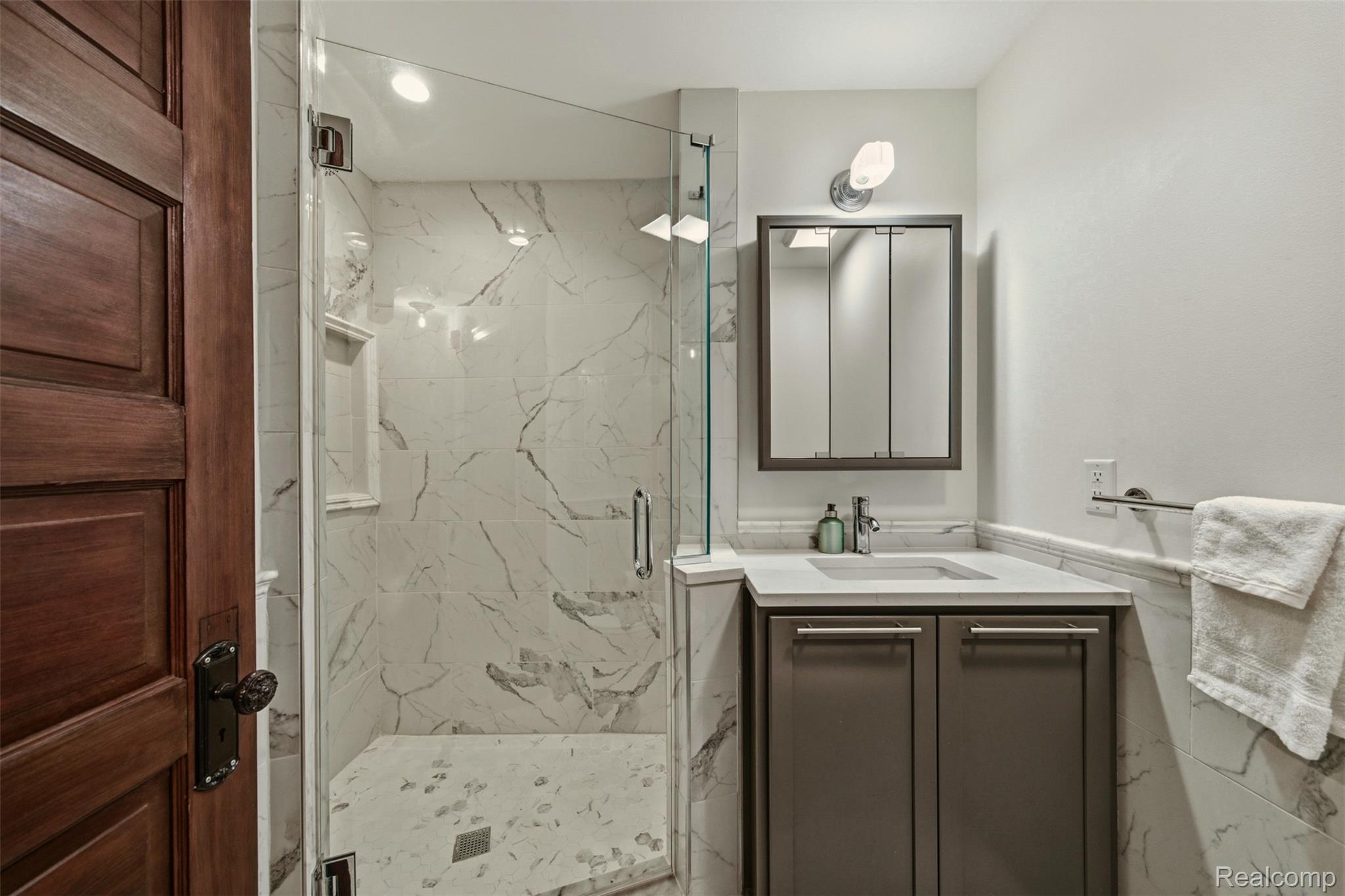 Bathroom with a glass walk-in shower, marble-look tile, and dark vanity.