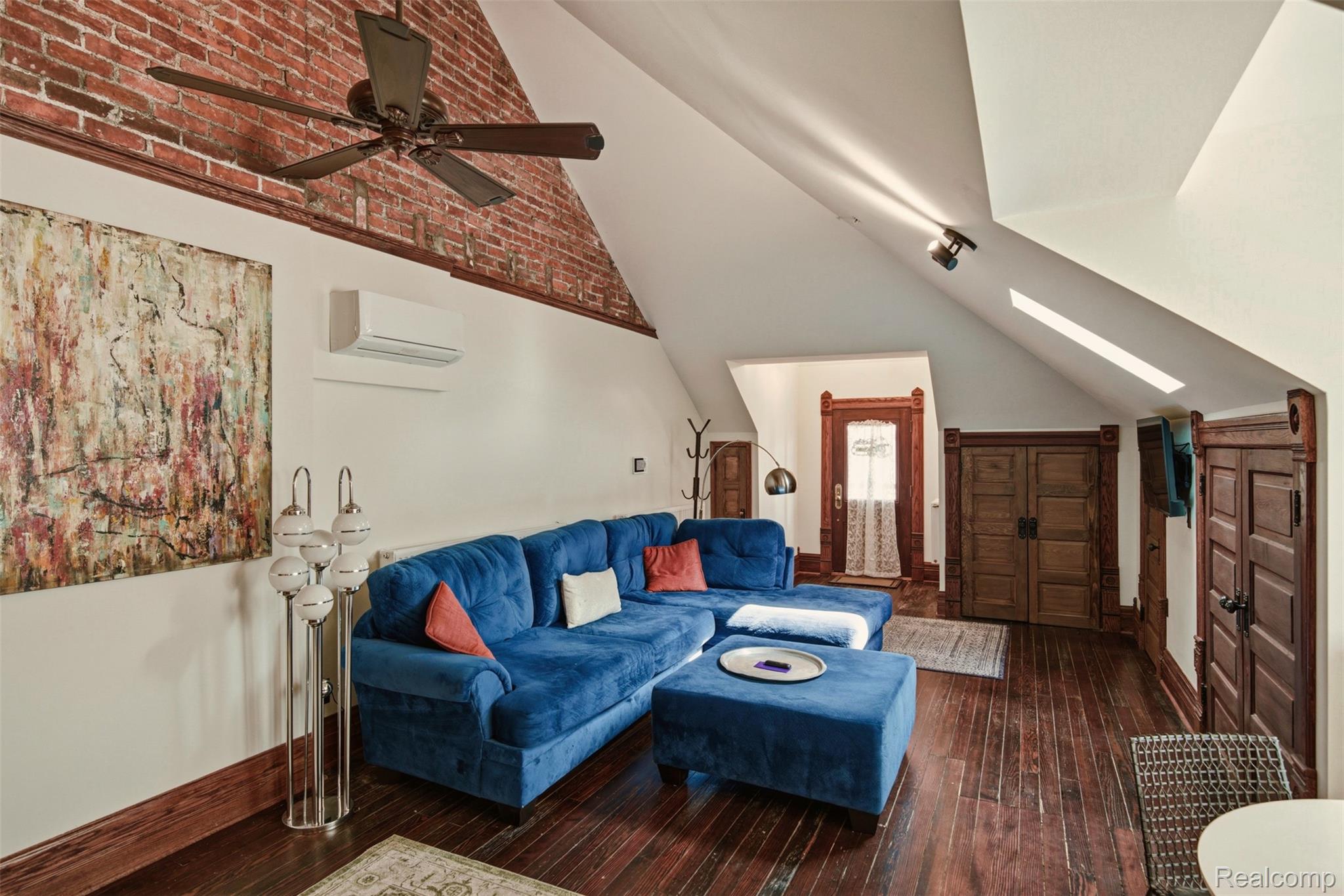 Loft living room with a blue sectional, exposed brick wall, and vaulted ceiling.