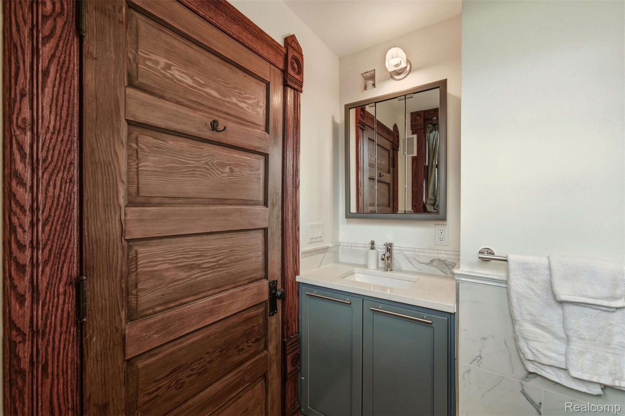 Bathroom vanity with a mirrored medicine cabinet beside an ornate dark wood door.