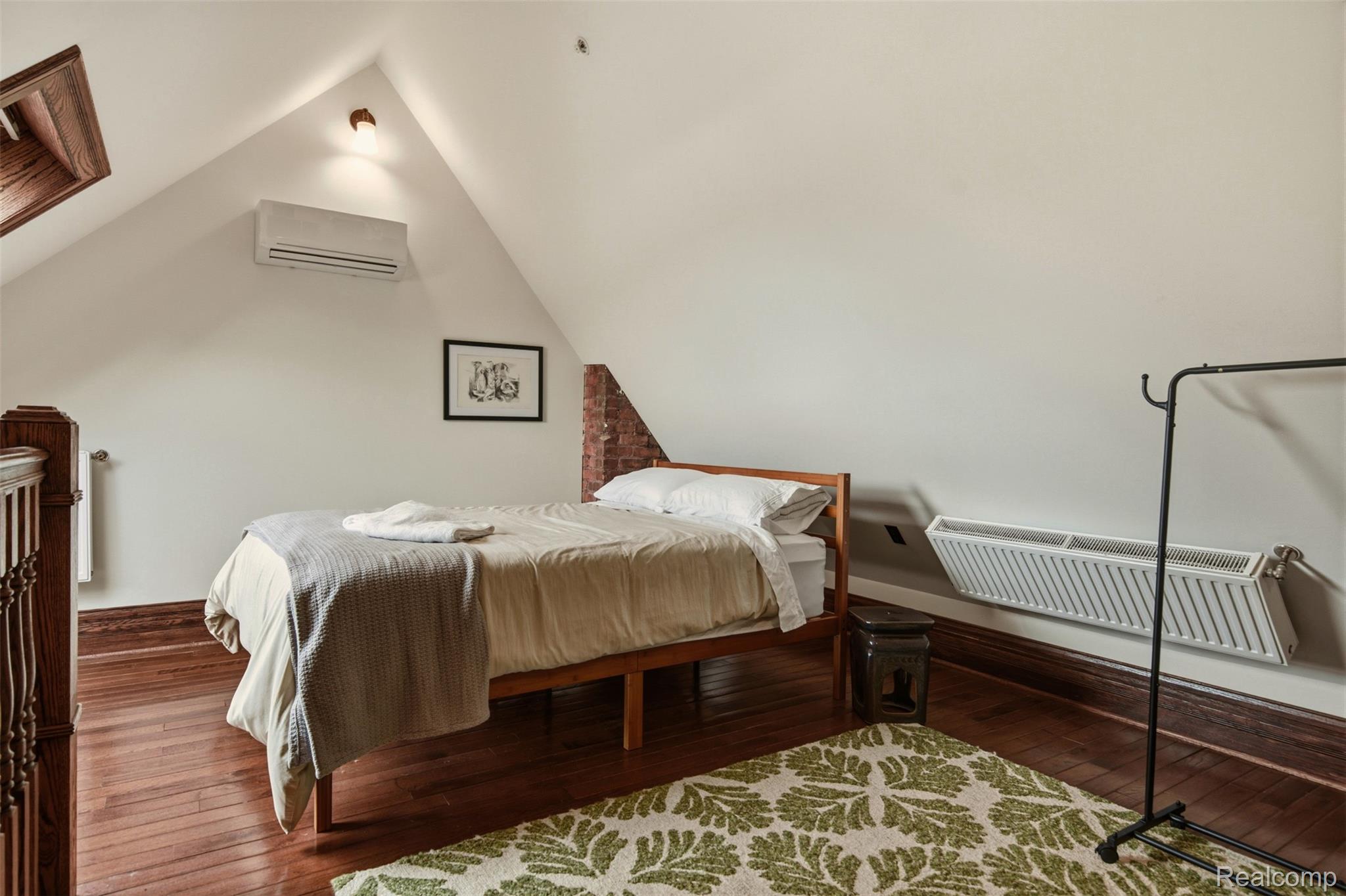 Furnished bedroom with a wooden bed beneath a sloped ceiling and a green patterned rug.