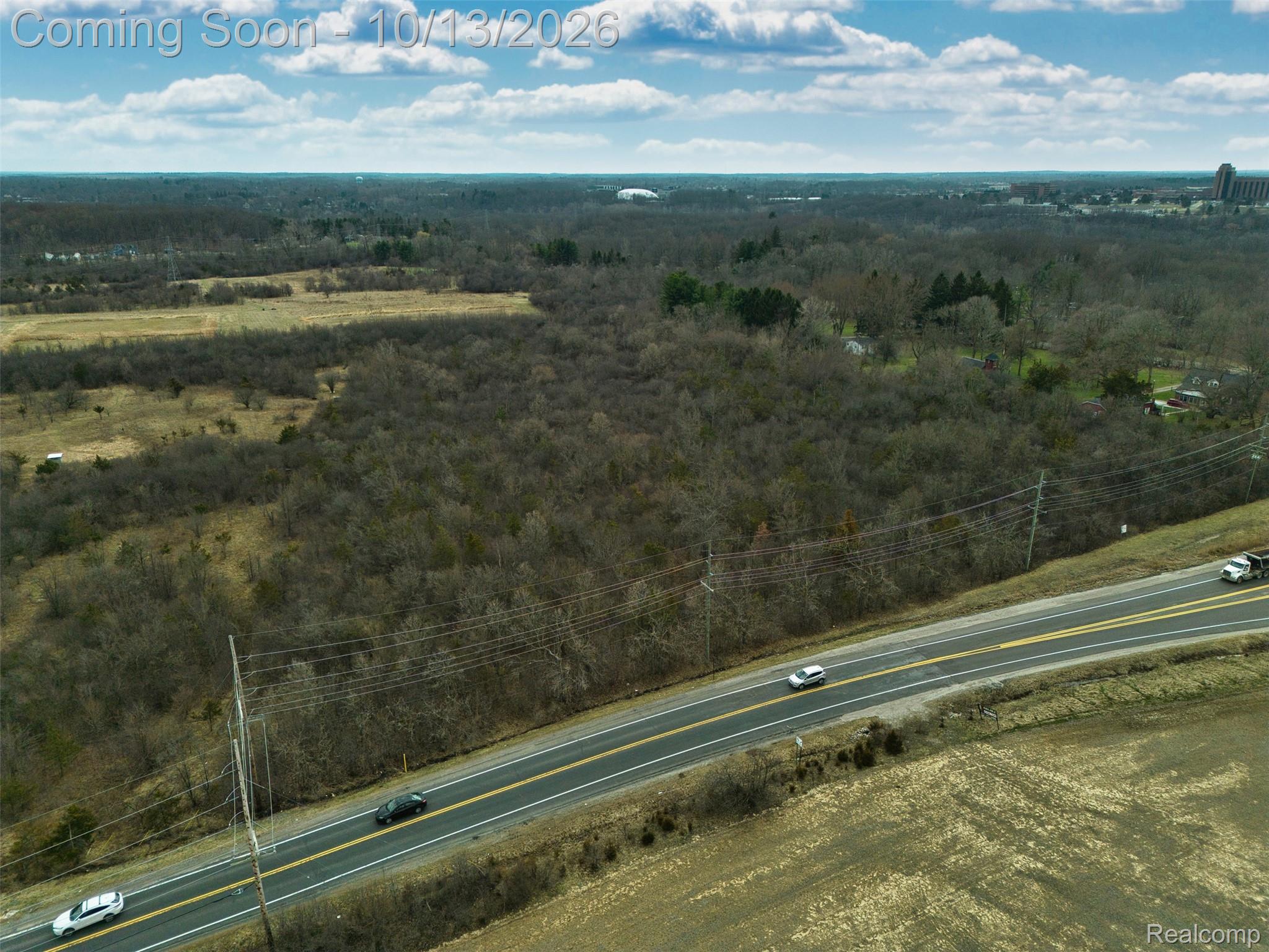 Aerial view of wooded and open land beside a two-lane road, with utility lines in the foreground.