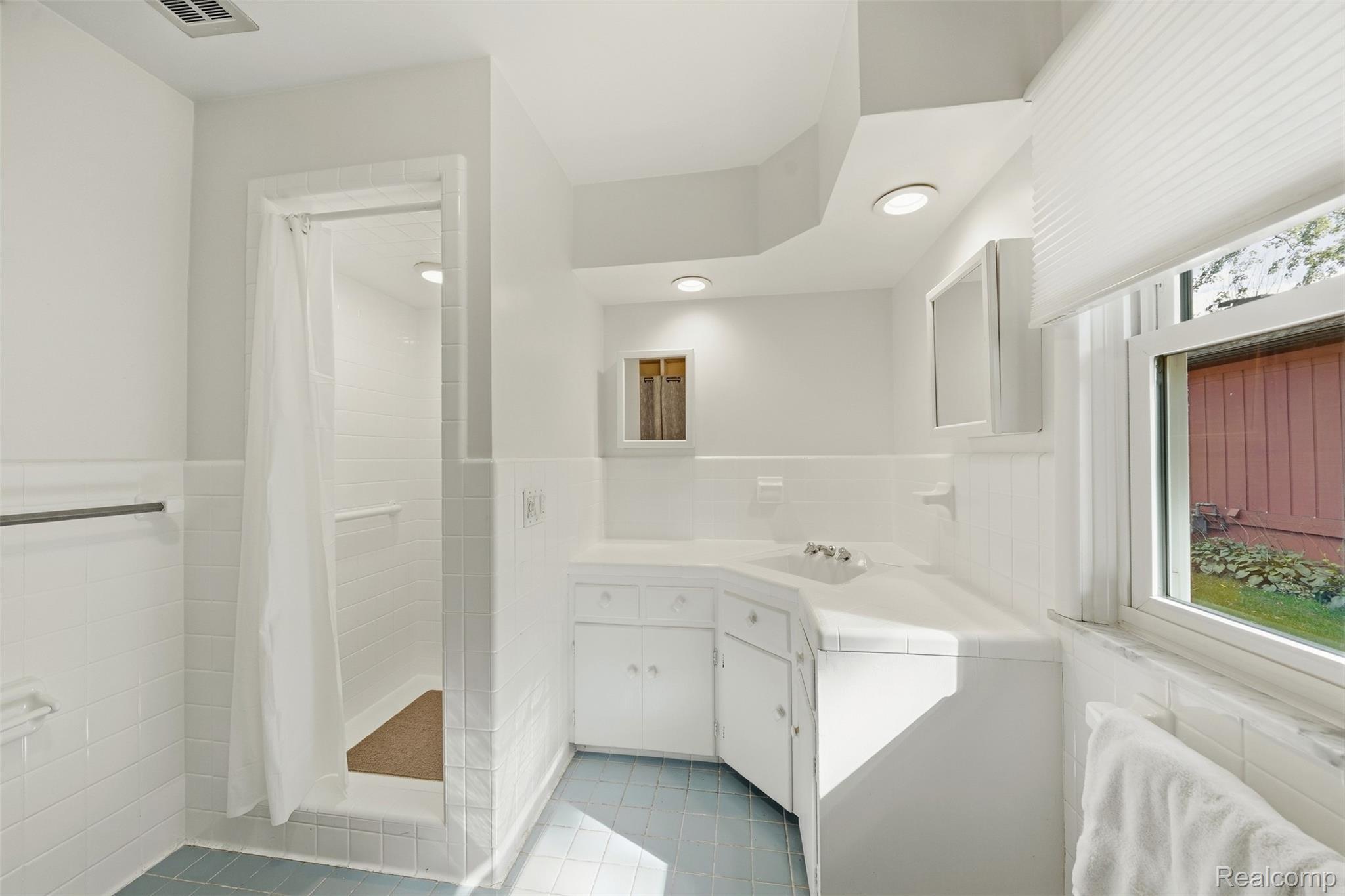 Bathroom with a corner vanity, tiled shower, blue floor tiles, and a large window.