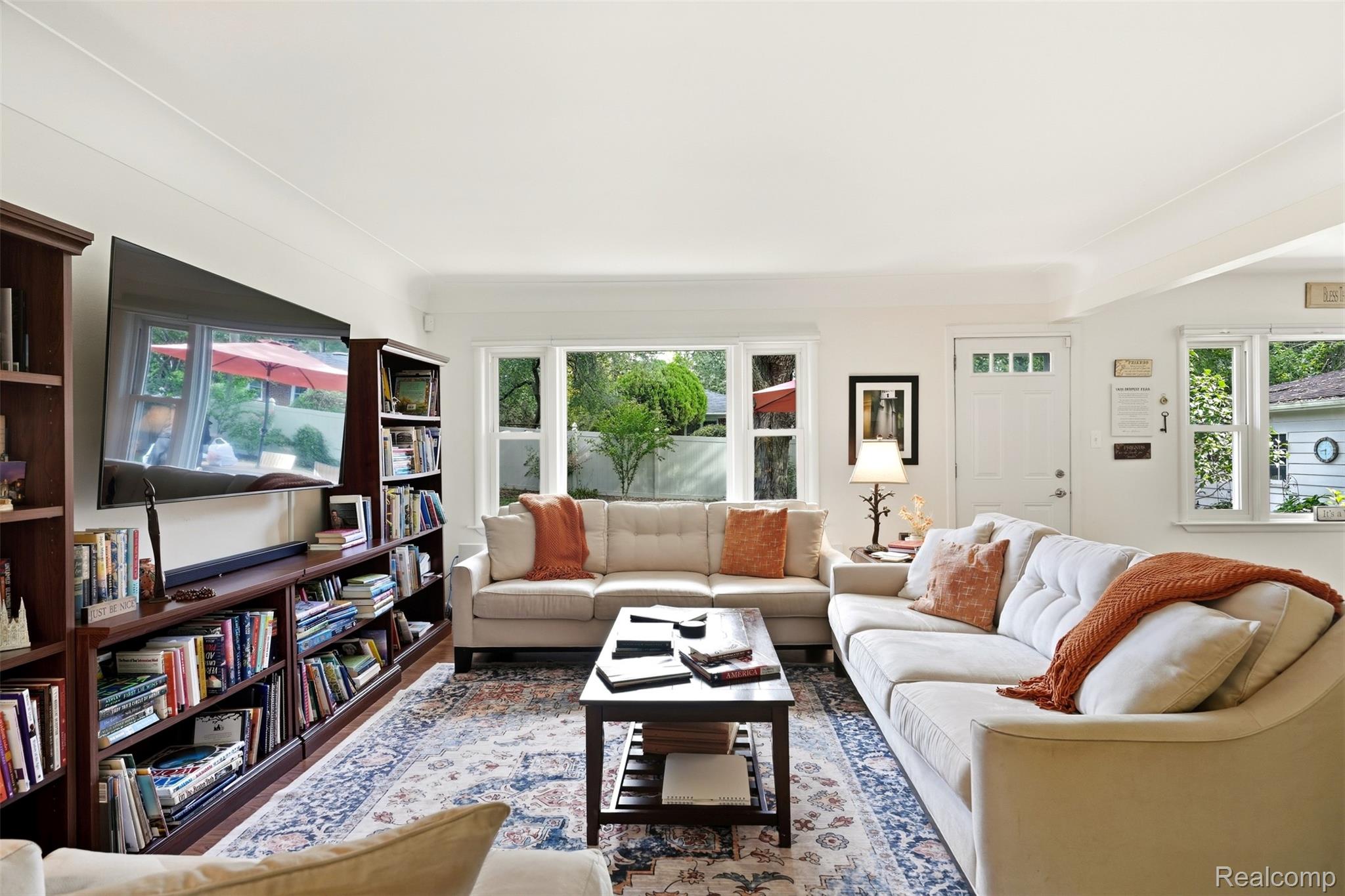 Living room with cream sofas, a full bookcase, patterned rug, and large garden-facing windows.