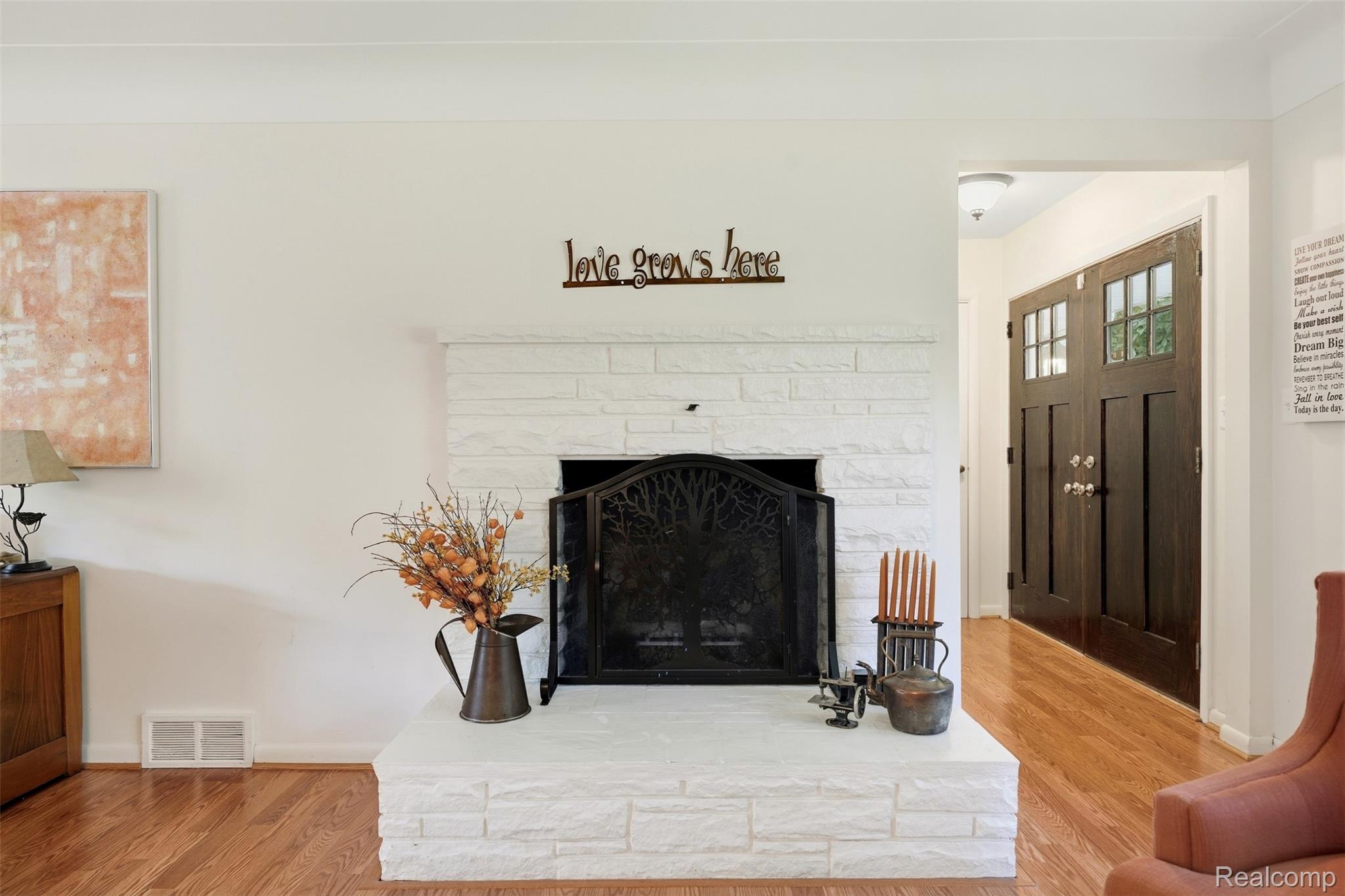 Living room with a white stone fireplace, black screen, hardwood floors, and dark double entry doors.