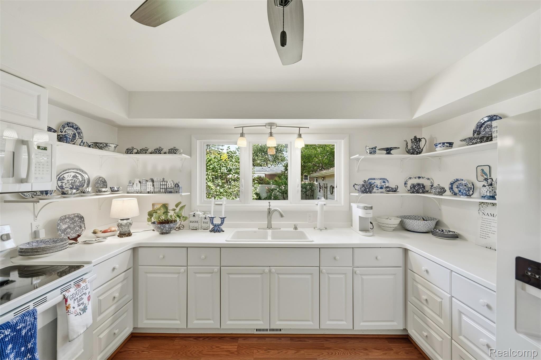White kitchen with blue-and-white china on open shelves and a sink beneath a wide window.