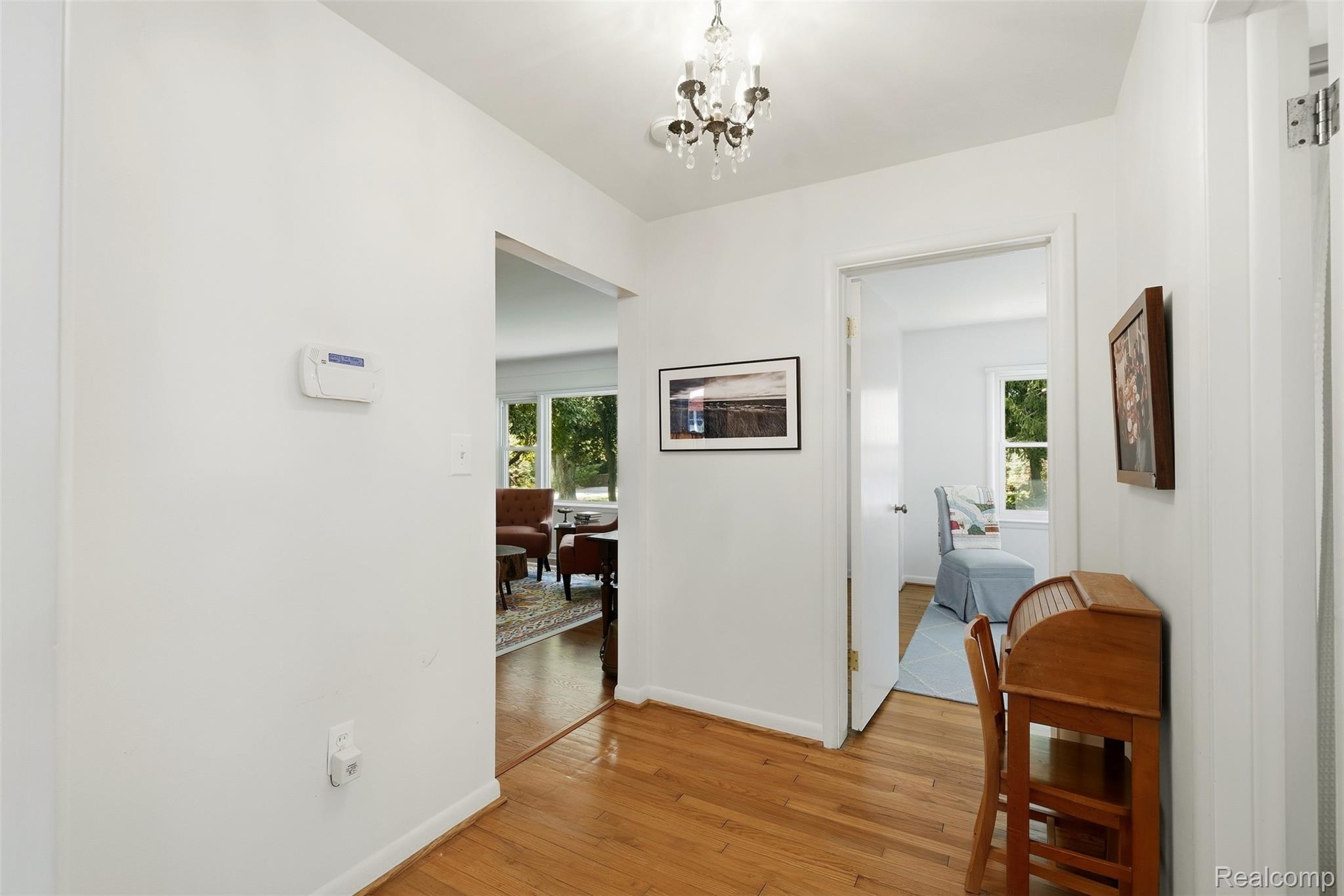 Furnished hallway with hardwood floors, a chandelier, and doorways to bright sitting areas.
