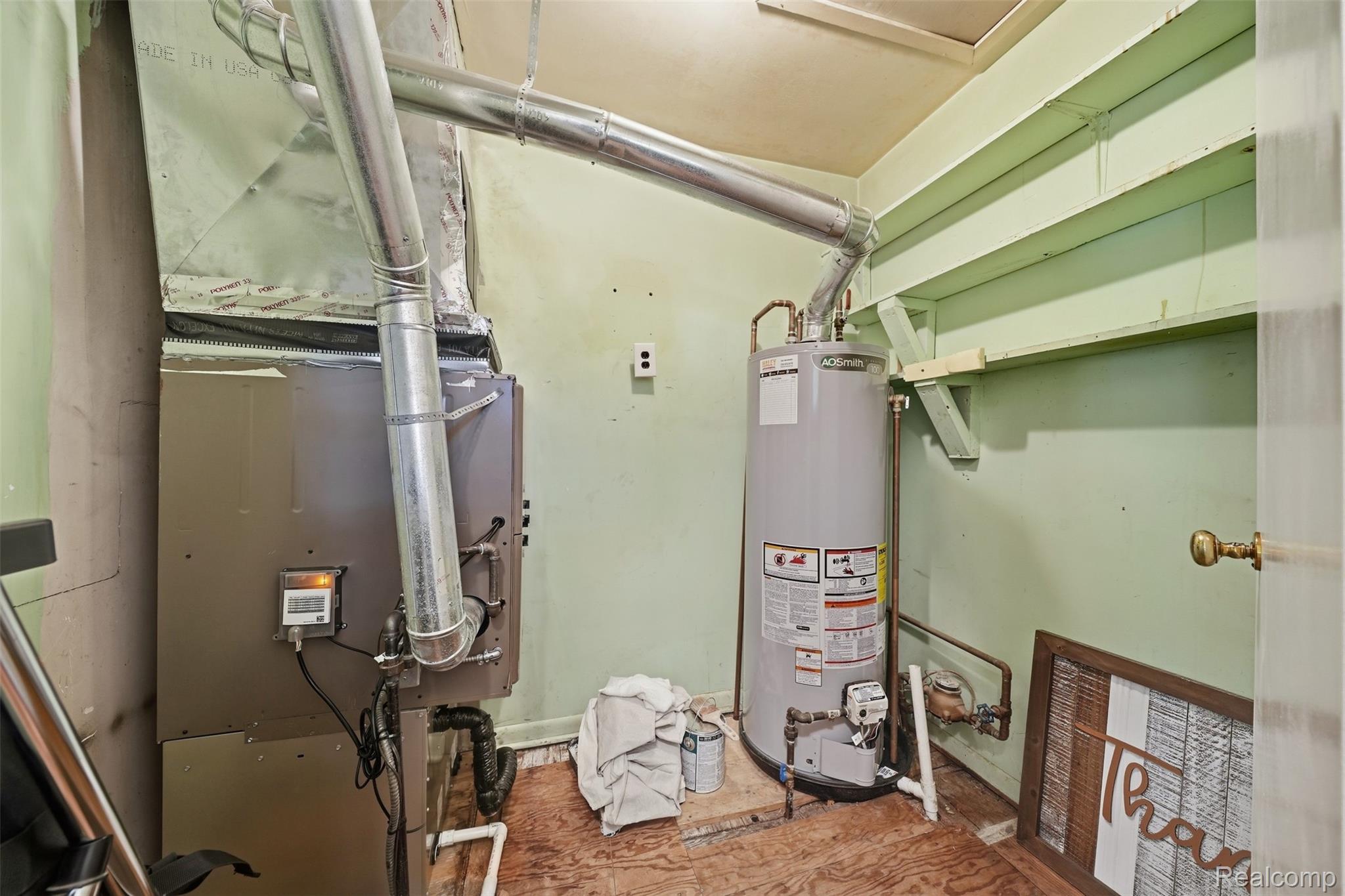 Utility room with a furnace, water heater, exposed ductwork, and plywood flooring.