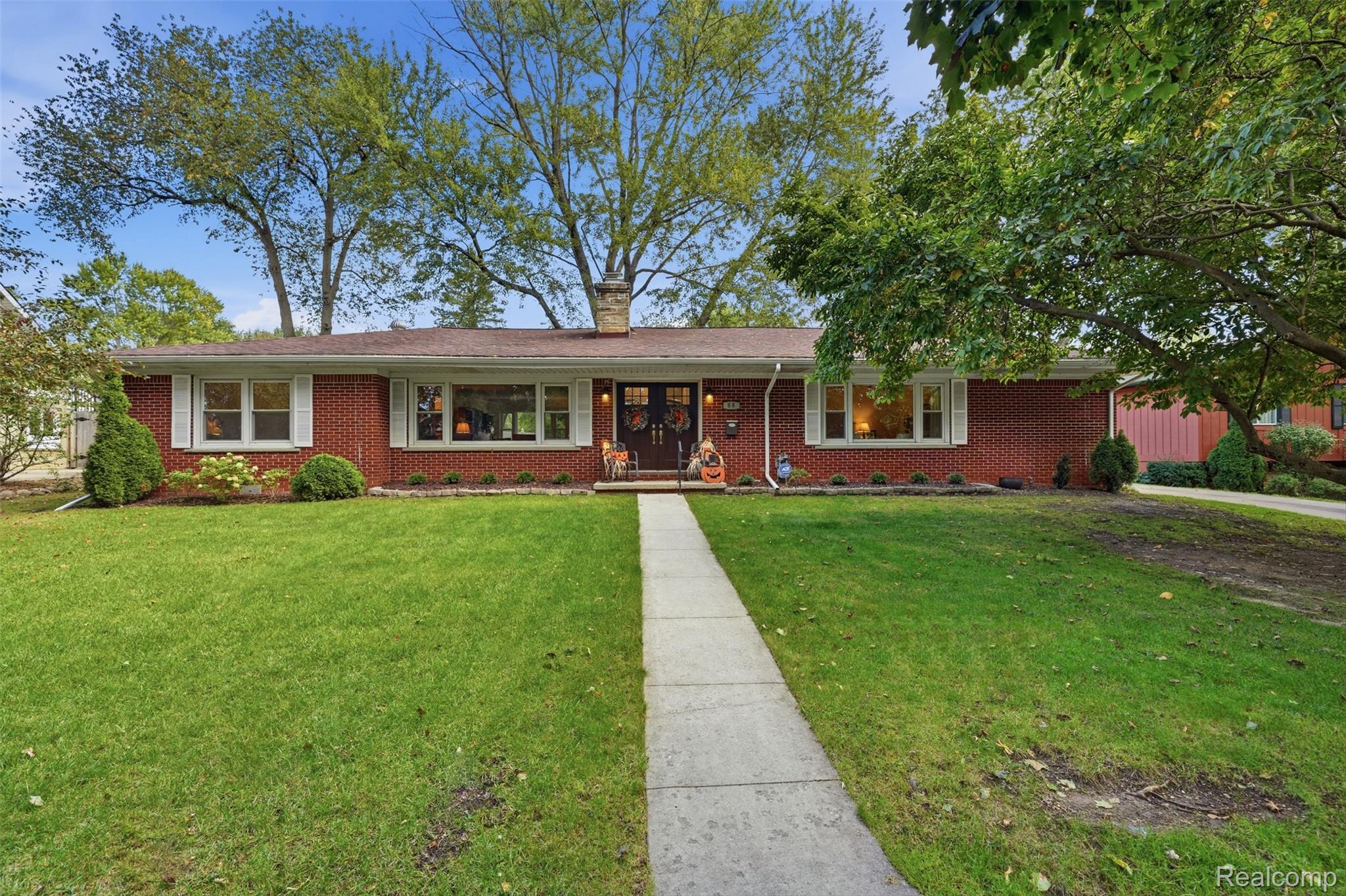 Single-story red brick house with a central entrance, concrete walkway, and mature trees.