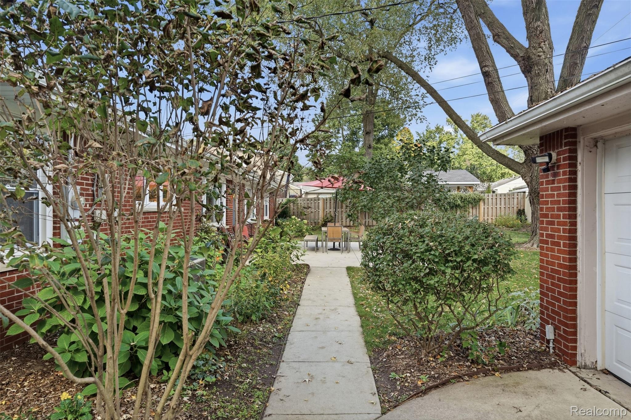 Landscaped courtyard with a walkway leading to patio seating beside a red brick home.