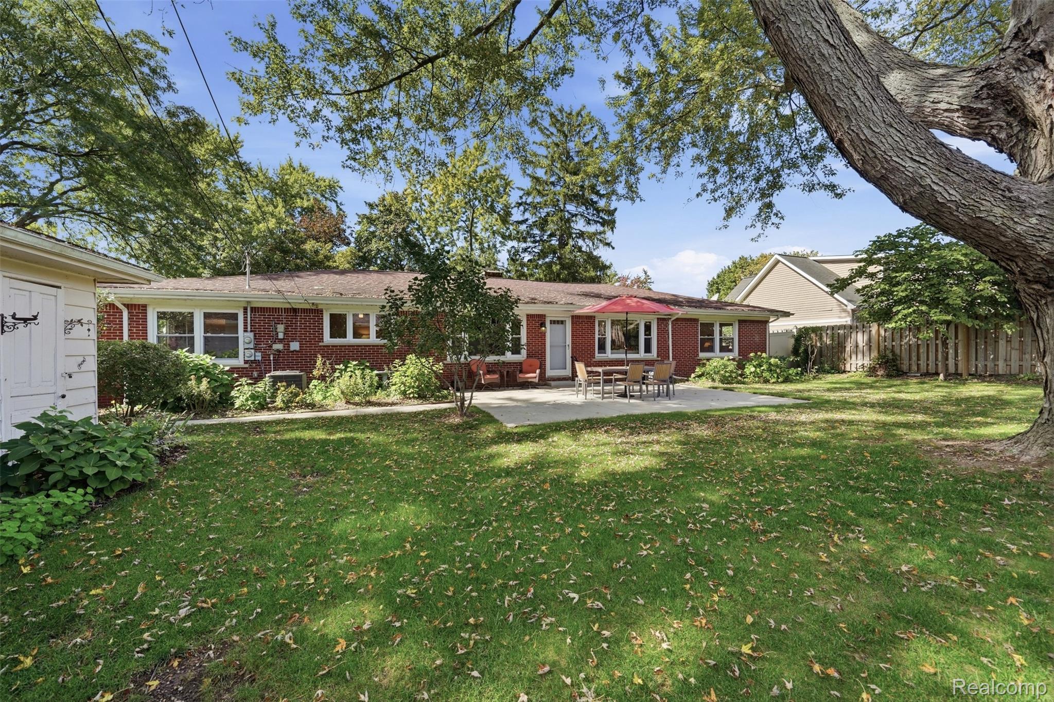 Single-story brick home with a shaded backyard lawn and patio dining area.