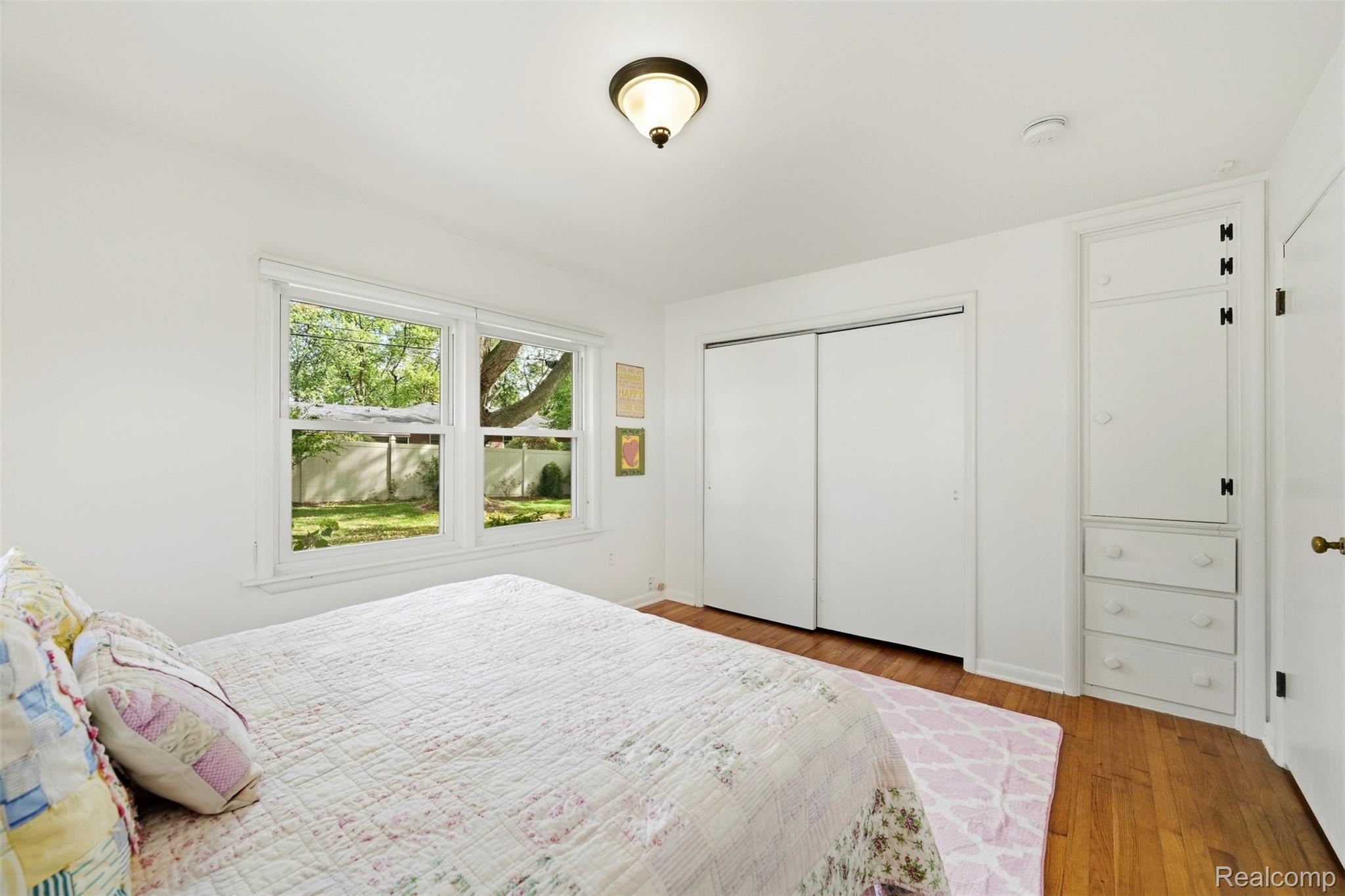 Bedroom with a floral quilt, two yard-facing windows, hardwood floors, and built-in storage.