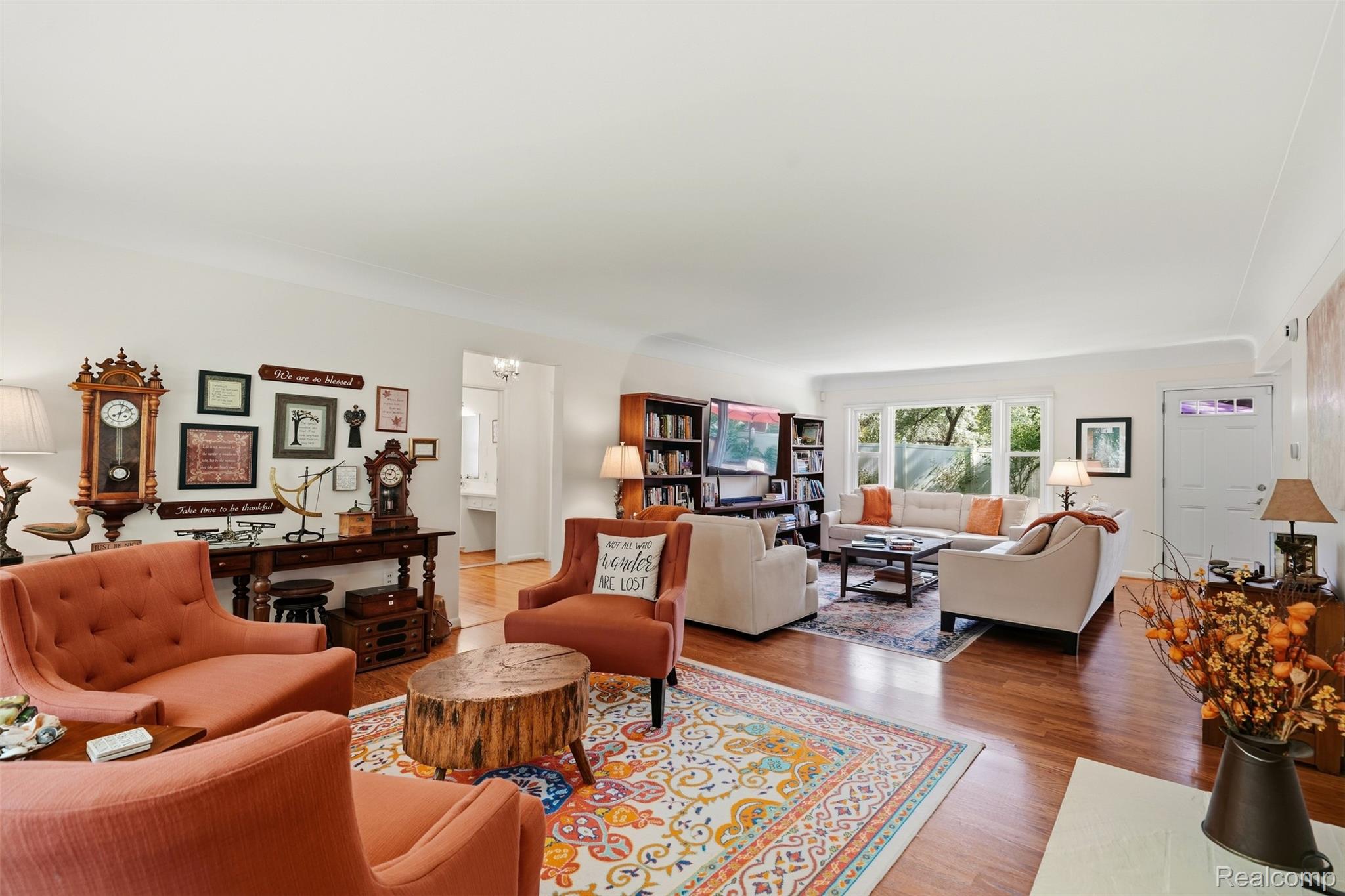 Furnished living room with rust-colored armchairs, cream sofas, bookshelves, and hardwood floors.