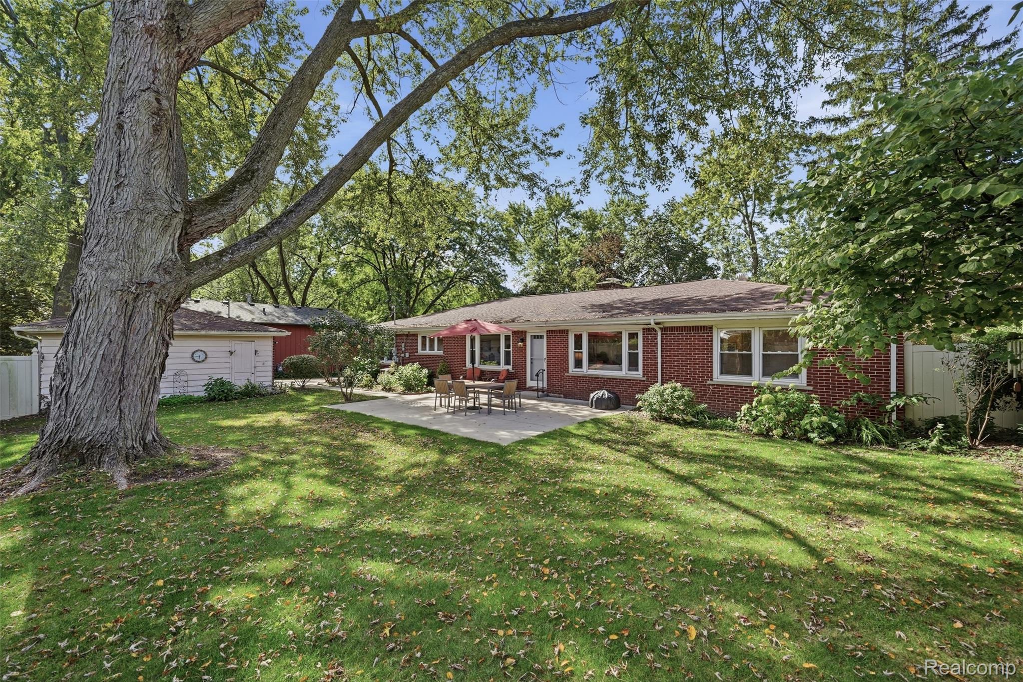 Red brick ranch home with a patio, detached garage, and large shade tree in the backyard.