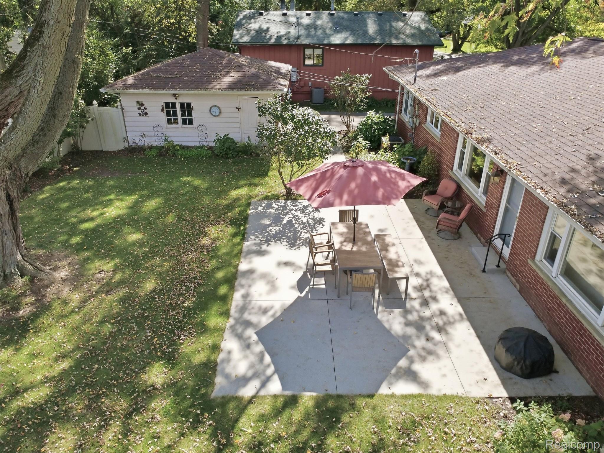 Backyard patio with outdoor dining set beneath a burgundy umbrella beside a brick home.