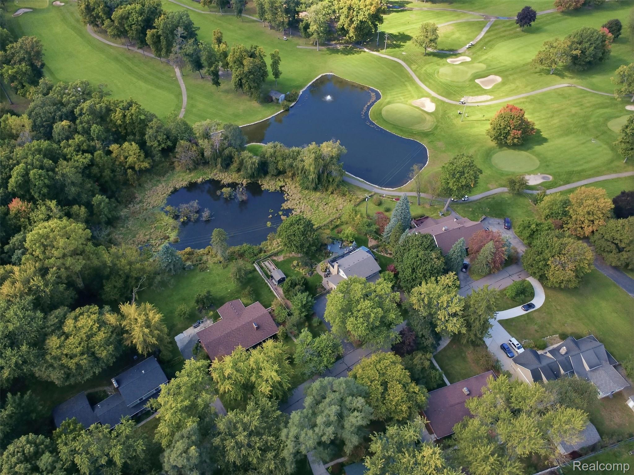Aerial view of homes beside a golf course, with two ponds and mature trees.
