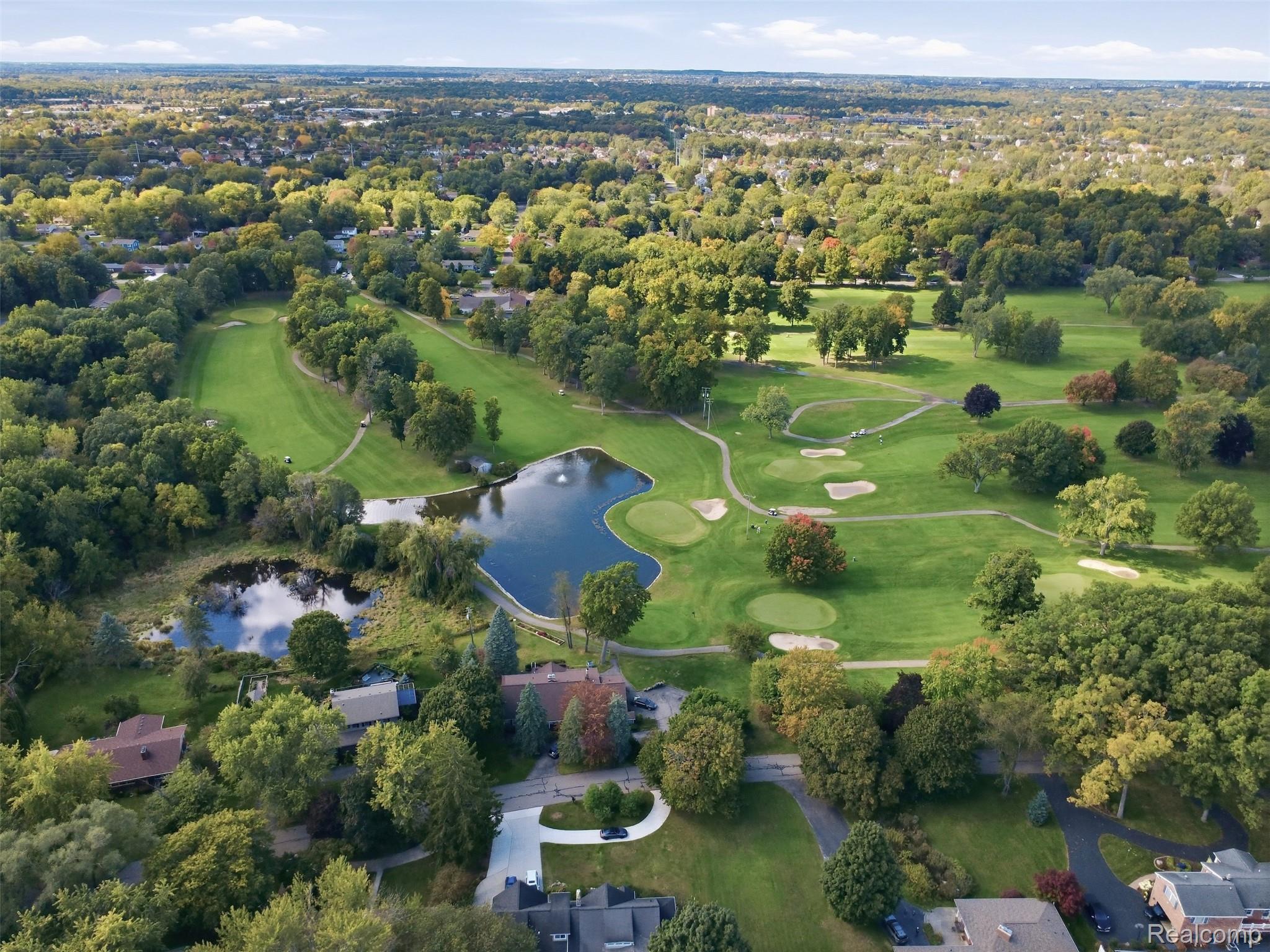 Aerial view of a golf course with ponds and wooded homes nearby.