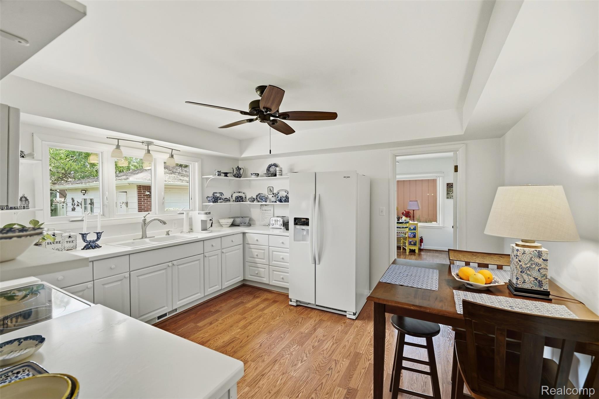 Bright white kitchen with hardwood floors, a window-side double sink, and a dark wood dining table.