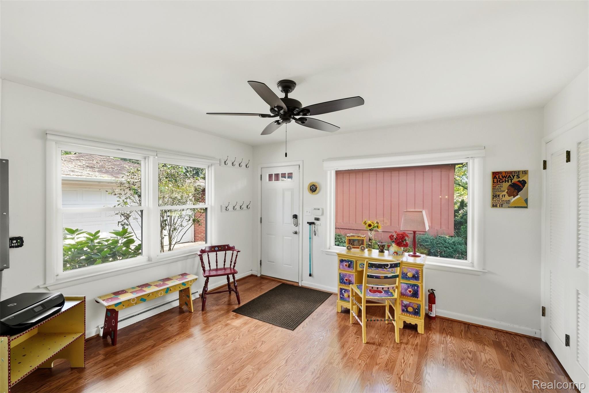 Bright sunroom with hardwood floors, wide windows, and colorful painted furniture.