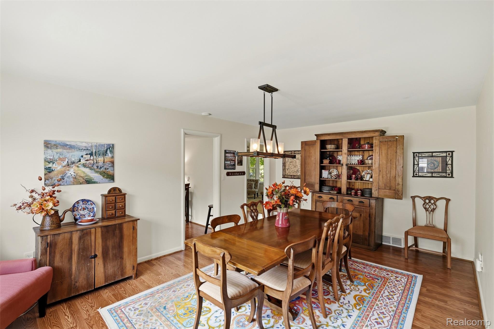 Dining room with a polished wood table, rustic china cabinet, and colorful patterned rug.