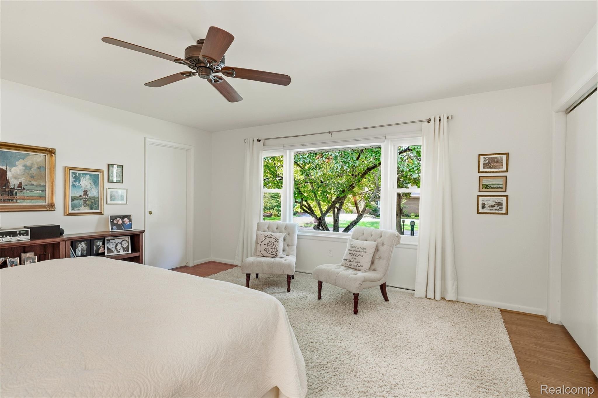 Bedroom with a large window overlooking leafy trees and two tufted chairs beside the bed.