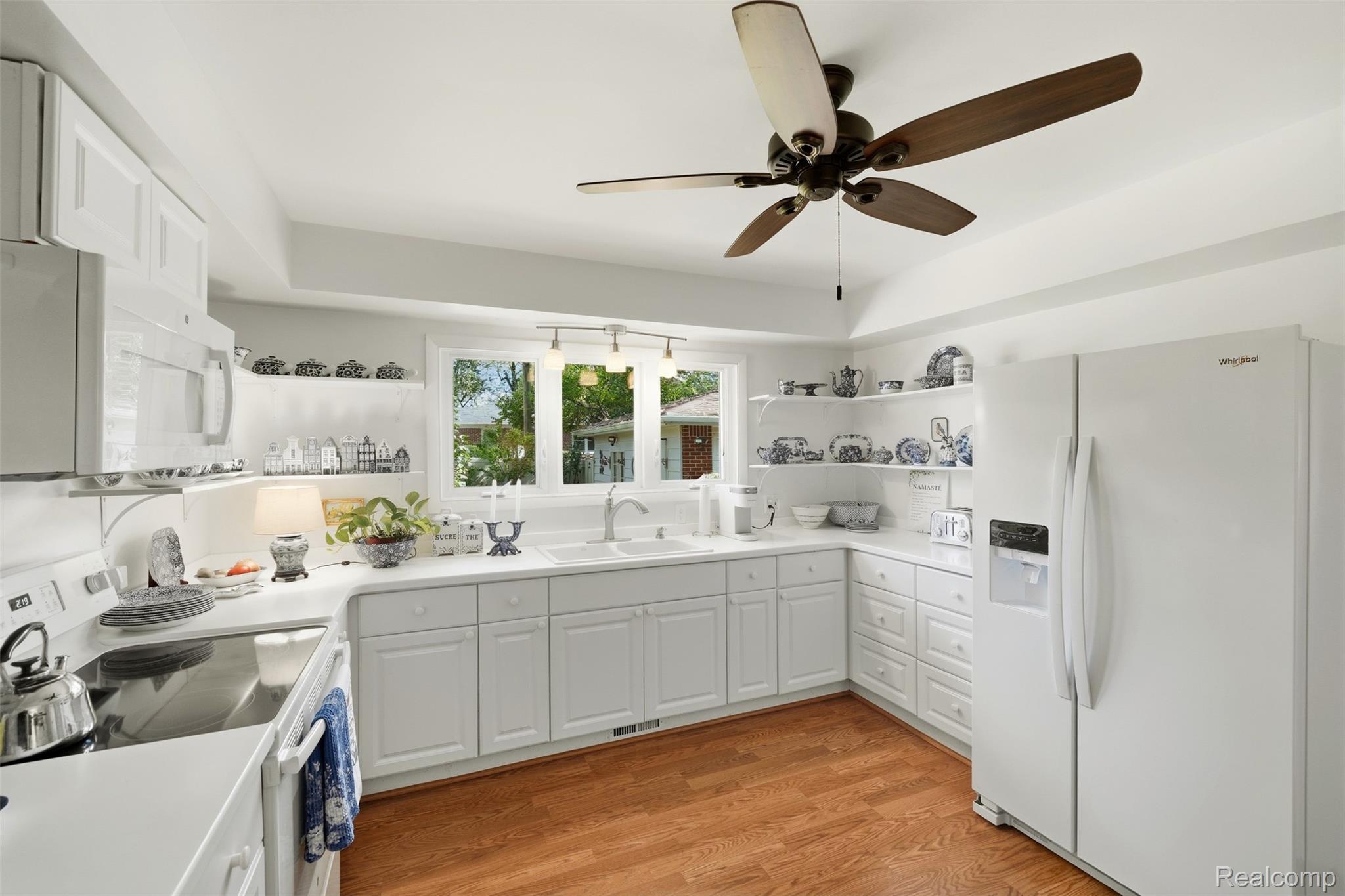 White kitchen with hardwood floors, open dish shelves, and a window above the sink.