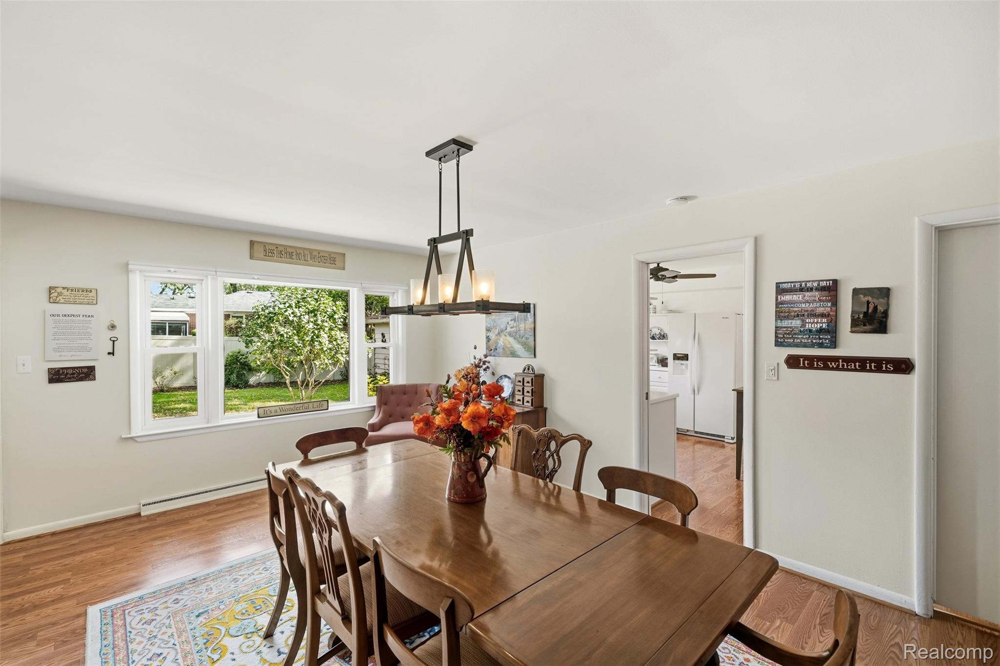Dining room with a large wooden table, chandelier, and wide windows overlooking a green yard.