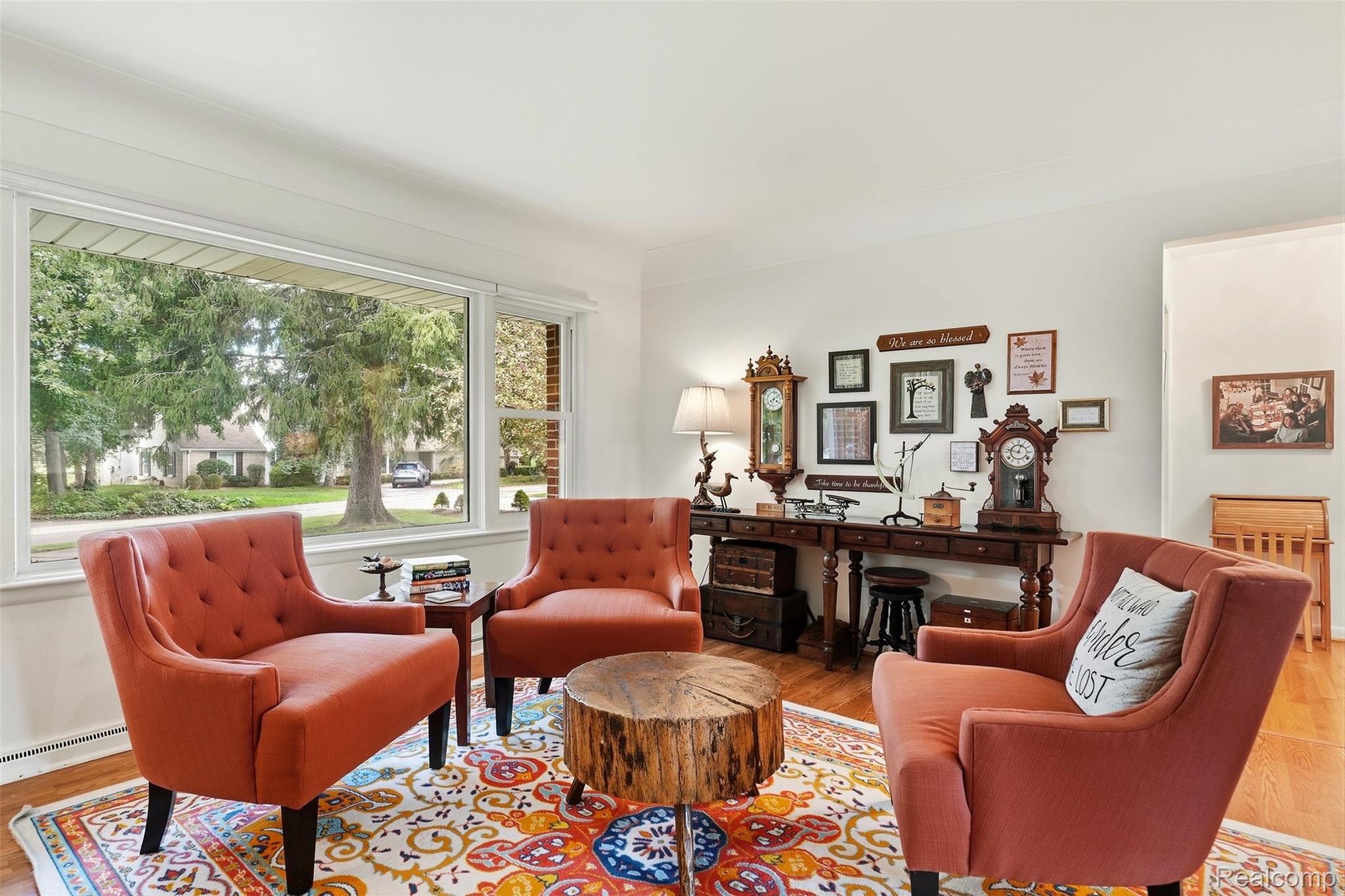 Living room with rust-colored armchairs, a stump coffee table, and a large window overlooking trees.