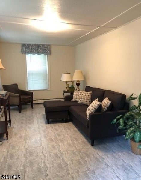 Living room with a dark sectional sofa, ottoman, patterned cushions, and tiled floor.