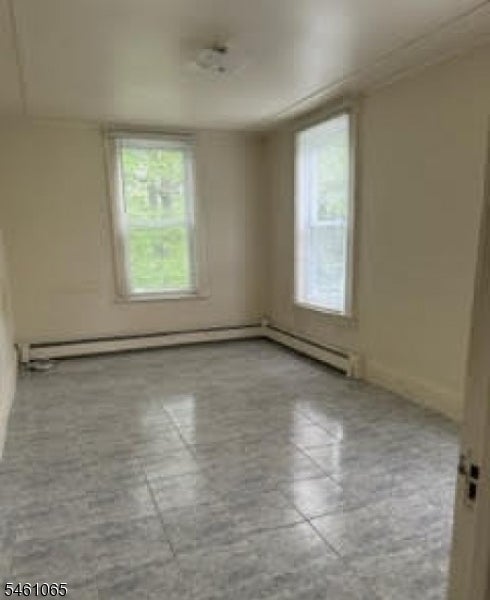 Empty room with a gray tiled floor, two windows, and baseboard radiators.