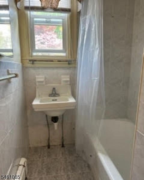 Bathroom with a wall-mounted sink beneath windows and a bathtub behind a shower curtain.