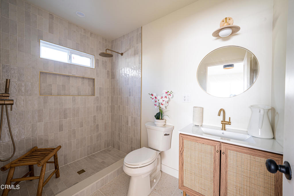 Bathroom with a tiled walk-in shower, woven-front vanity, and oval mirror.