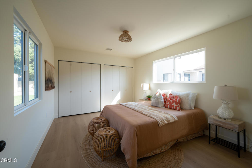 Staged bedroom with a brown bed, white closets, and large windows.