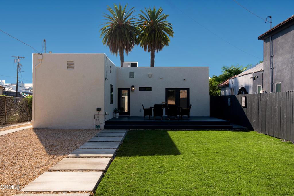 Modern home's backyard with a green lawn, gravel path, patio furniture, and two palm trees.
