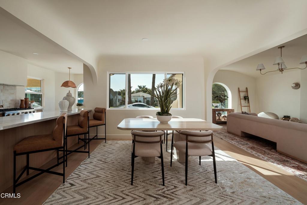 Dining area with a long table, patterned rug, and open view to the kitchen and living room.