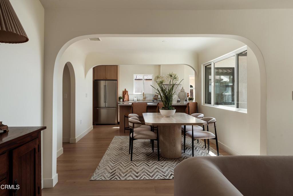 Dining area with a wood table and upholstered chairs, opening into a kitchen with stainless steel appliances.