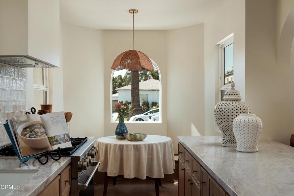 Bright kitchen with marble countertops, wood cabinetry, and an arched window beneath a woven pendant light.