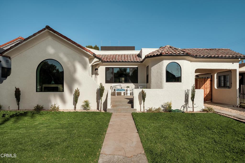 Stucco house with a tile roof, arched windows, cactus landscaping, and a walkway through the front lawn.