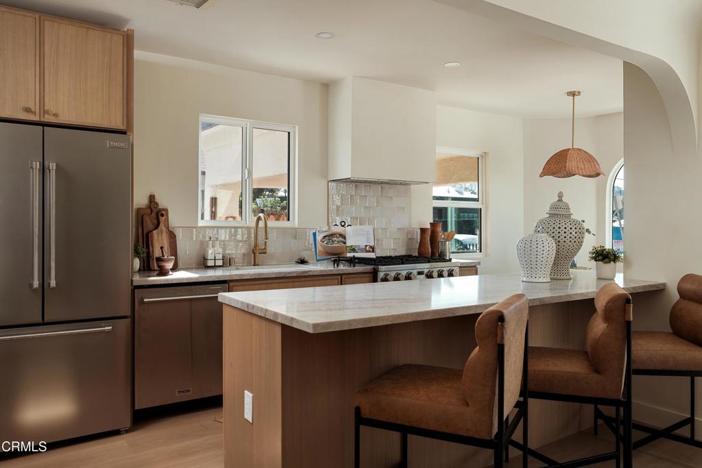 Kitchen with a large island, wood cabinetry, stainless steel refrigerator, and upholstered counter stools.